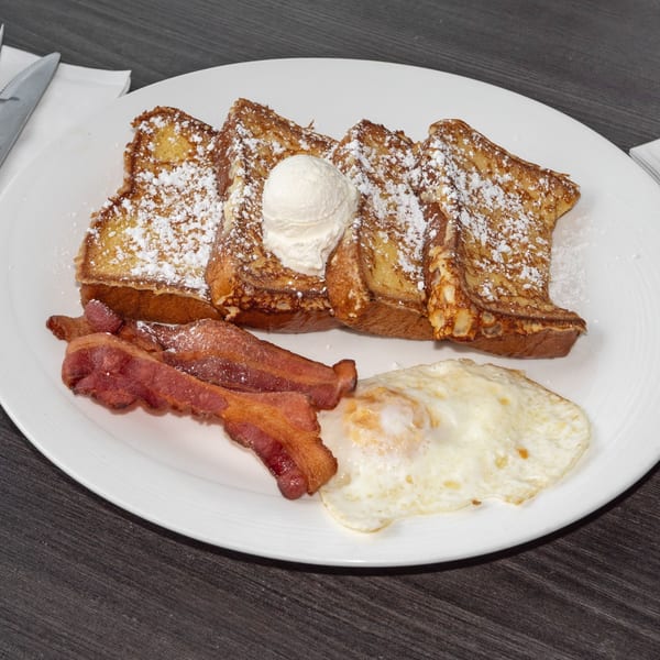 French toast with powdered sugar, a scoop of ice cream, bacon, and a fried egg on a white plate.