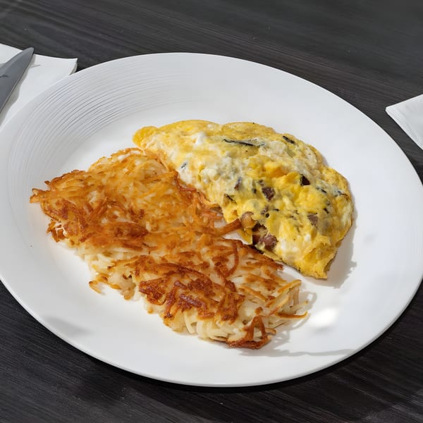 A fluffy omelet with hash browns on a white plate, ready for a delicious breakfast.